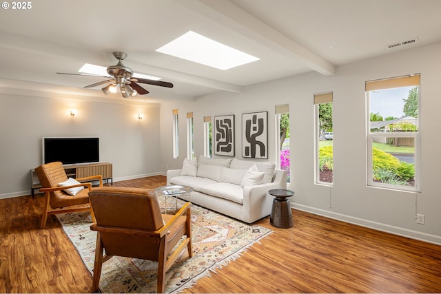 living area featuring a skylight, baseboards, wood finished floors, and beam ceiling
