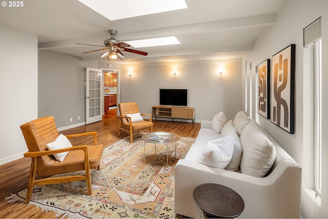 living area with a skylight, baseboards, wood finished floors, and a ceiling fan