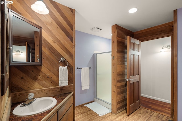 bathroom with a shower stall, vanity, wood finished floors, wood walls, and baseboards