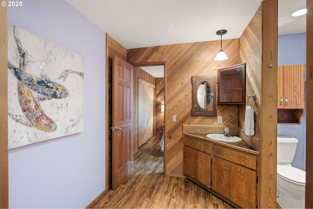 bathroom with wood walls, toilet, wood finished floors, and vanity