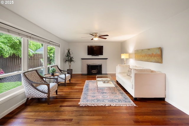 living room with ceiling fan, baseboards, wood finished floors, and a brick fireplace