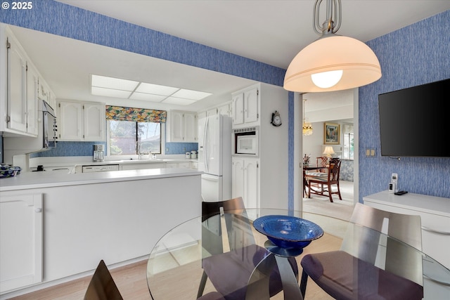 kitchen with decorative light fixtures, wallpapered walls, white appliances, a peninsula, and light countertops