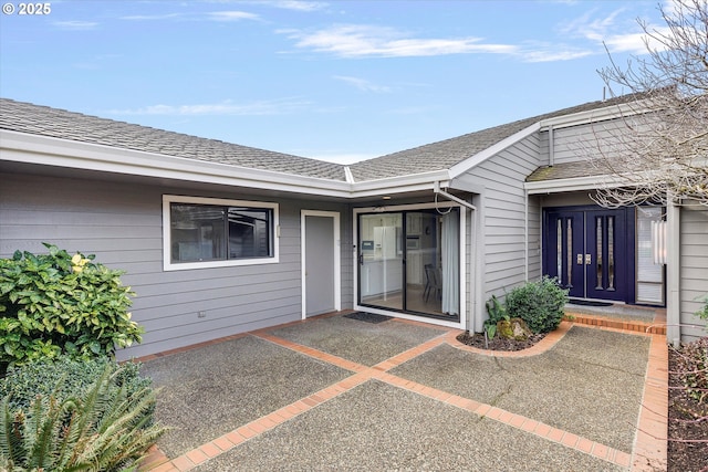 entrance to property with a patio and a shingled roof