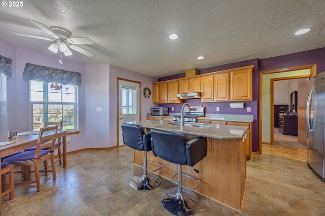 788 SE Meadows Loop, Sheridan, OR 97378 - kitchen with an island with sink, stainless steel appliances, under cabinet range hood, a sink, and a textured ceiling