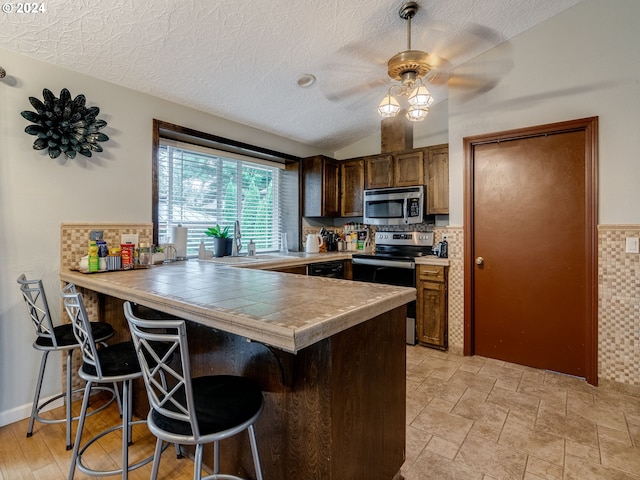 kitchen featuring appliances with stainless steel finishes, lofted ceiling, sink, a kitchen breakfast bar, and kitchen peninsula