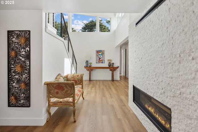 living area with a towering ceiling, a glass covered fireplace, light wood-style flooring, and baseboards