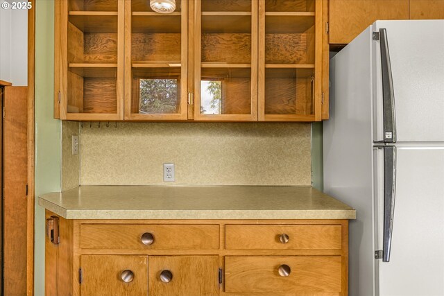 1220 NE 196th Ave, Portland, OR 97230 - kitchen with freestanding refrigerator, glass insert cabinets, brown cabinetry, light countertops, and decorative backsplash