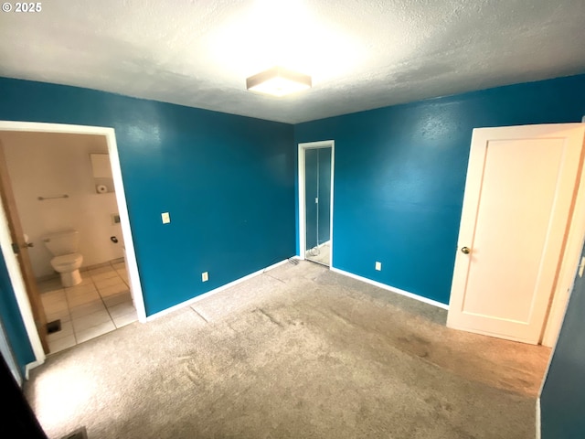 unfurnished bedroom with carpet flooring, ensuite bathroom, and a textured ceiling