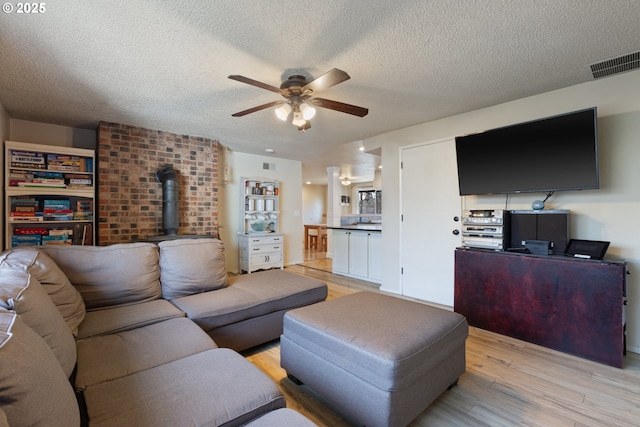 living room featuring ceiling fan, light hardwood / wood-style floors, a textured ceiling, and a wood stove