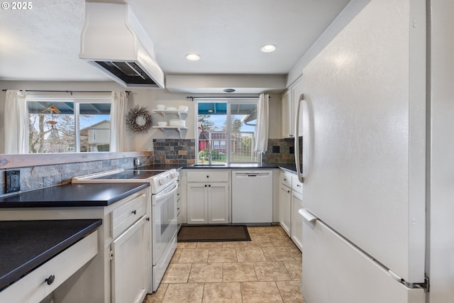 kitchen with tasteful backsplash, white cabinetry, sink, custom range hood, and white appliances