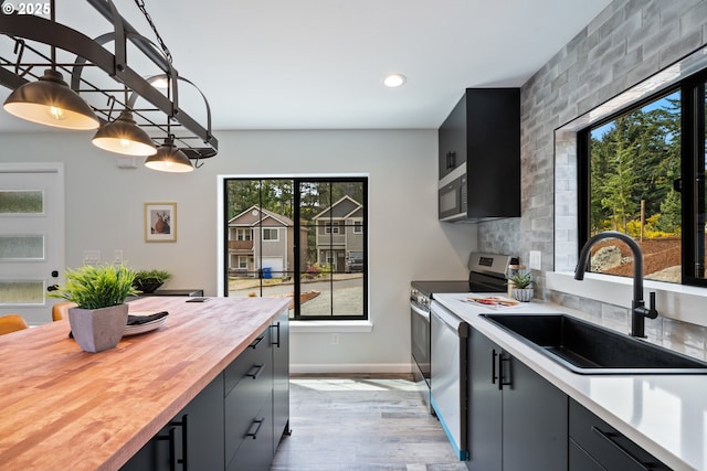 kitchen with a sink, butcher block counters, stainless steel range with electric stovetop, light wood-style floors, and decorative light fixtures