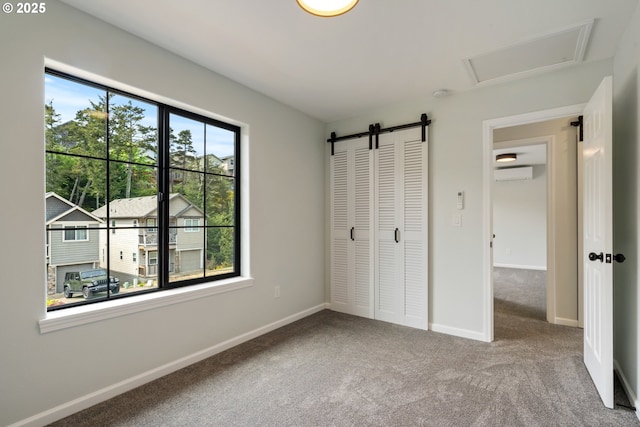 unfurnished bedroom featuring a wall mounted AC, carpet flooring, baseboards, a closet, and a barn door