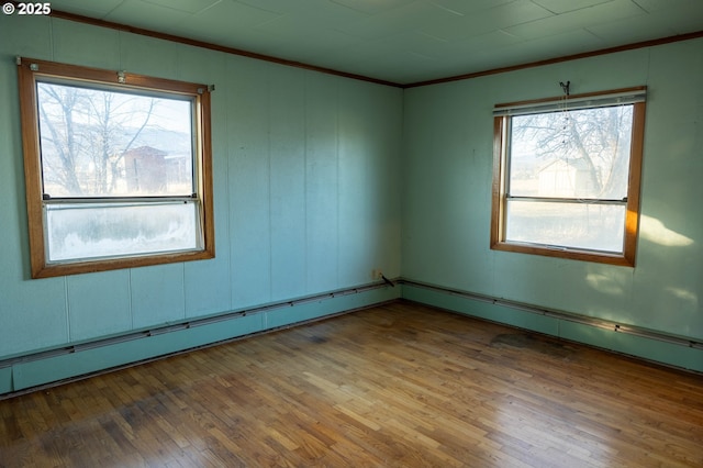 unfurnished room with a baseboard heating unit, wood finished floors, and crown molding