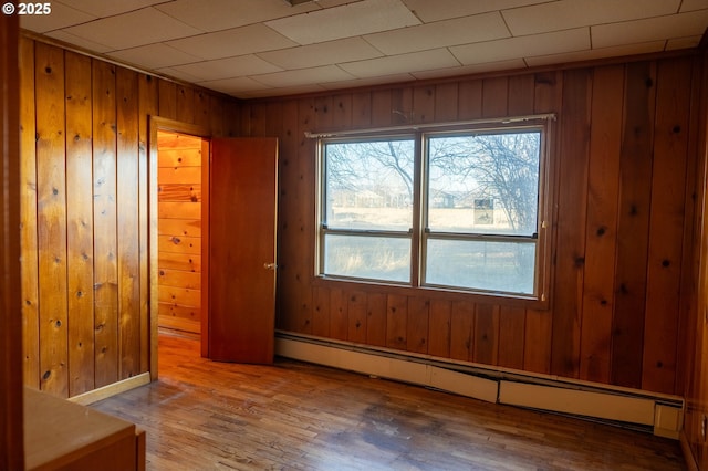 empty room with wooden walls, a baseboard heating unit, and wood finished floors