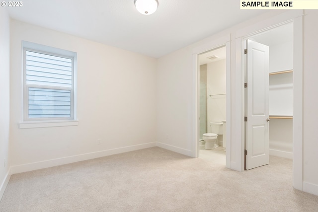 unfurnished bedroom featuring light carpet, ensuite bath, a walk in closet, and a closet