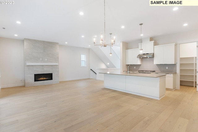 kitchen with tasteful backsplash, hanging light fixtures, an island with sink, light hardwood / wood-style floors, and white cabinets