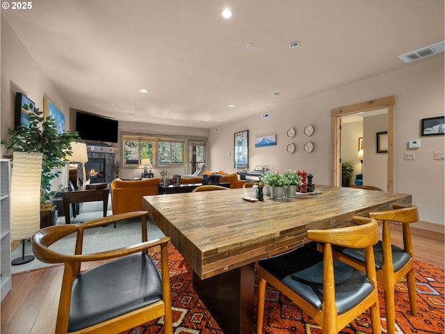 dining area featuring light wood-style flooring, a lit fireplace, and recessed lighting