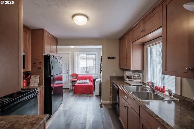 kitchen featuring dark countertops, wood finished floors, brown cabinetry, black appliances, and a sink