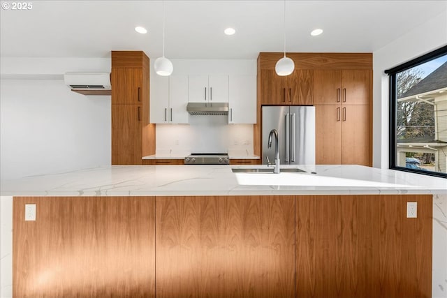 kitchen with white cabinets, appliances with stainless steel finishes, under cabinet range hood, pendant lighting, and a sink