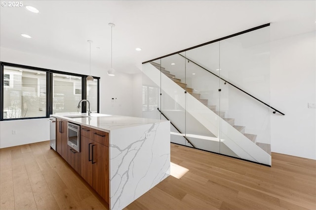 kitchen with decorative light fixtures, brown cabinetry, a sink, modern cabinets, and light wood-type flooring