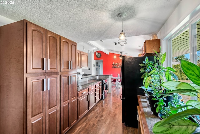 kitchen featuring dark wood finished floors, lofted ceiling, decorative light fixtures, freestanding refrigerator, and stainless steel range with electric stovetop