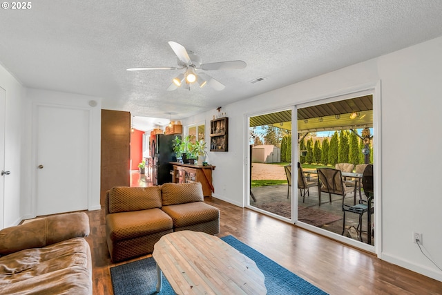 living area with a textured ceiling, ceiling fan, wood finished floors, visible vents, and baseboards