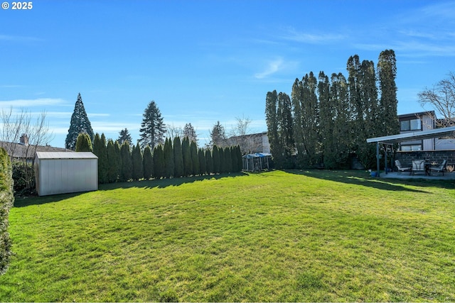 view of yard featuring a patio area, fence, a storage unit, and an outbuilding