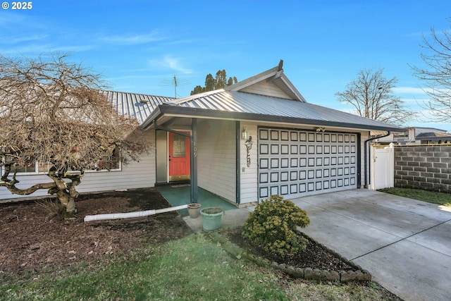 view of front of house with a garage, concrete driveway, metal roof, and fence