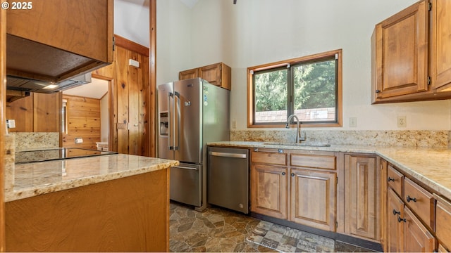 kitchen with a sink, a towering ceiling, brown cabinets, light stone countertops, and appliances with stainless steel finishes