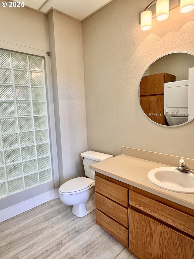 bathroom featuring hardwood / wood-style flooring, stacked washer and clothes dryer, toilet, and vanity