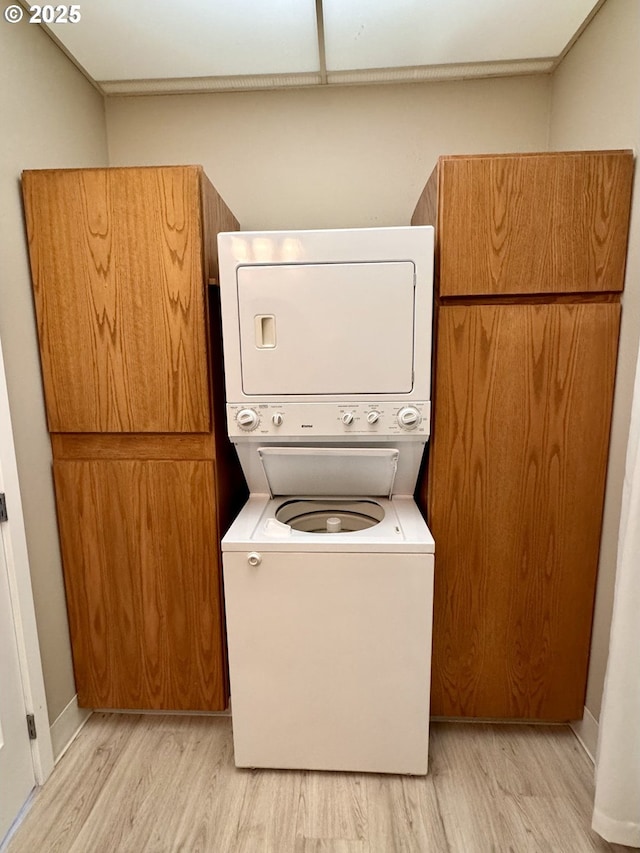 laundry area featuring cabinets, stacked washer / drying machine, and light hardwood / wood-style floors