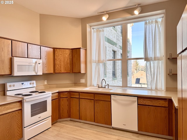 kitchen featuring white appliances, rail lighting, sink, and light hardwood / wood-style flooring