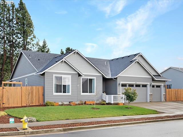 craftsman-style house featuring concrete driveway, roof with shingles, an attached garage, fence, and a front lawn