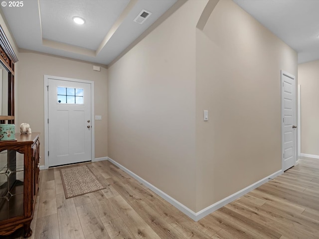 entrance foyer featuring arched walkways, visible vents, baseboards, light wood finished floors, and a raised ceiling