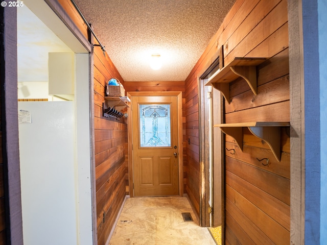 entryway with a textured ceiling and wood walls