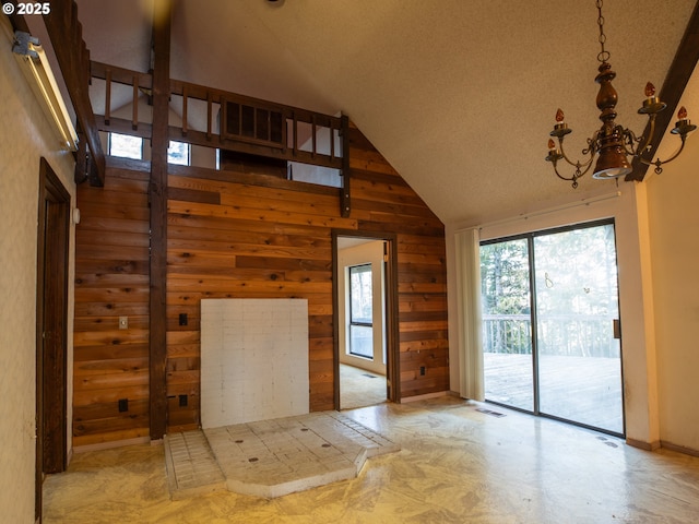 unfurnished living room with high vaulted ceiling, an inviting chandelier, and wooden walls