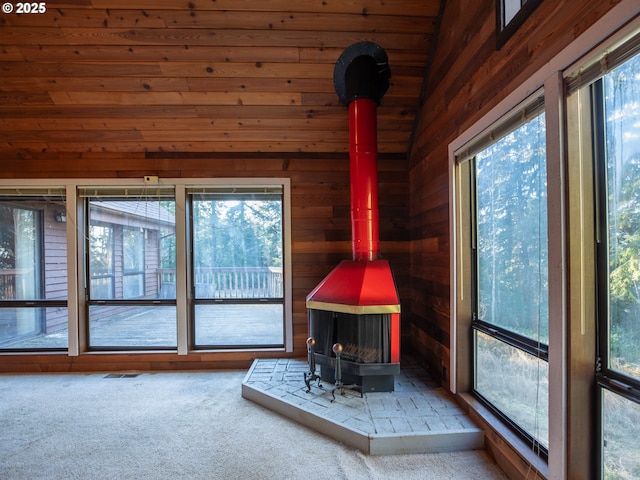 unfurnished living room featuring wooden walls, carpet floors, and a wood stove