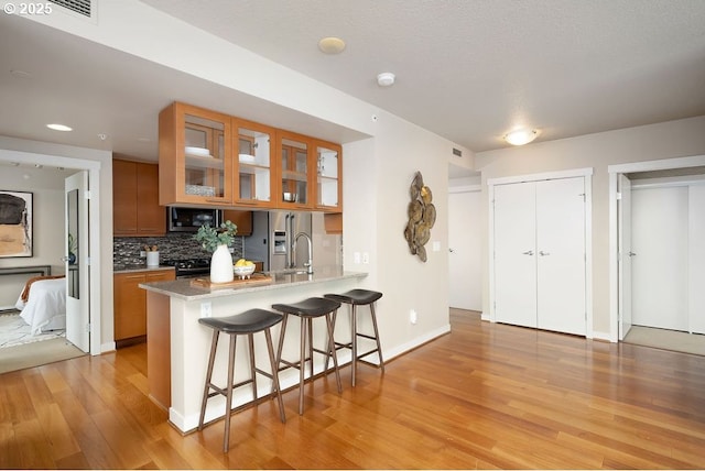 1500 SW 11th Ave Unit 2404, Portland, OR 97201 - kitchen with appliances with stainless steel finishes, brown cabinetry, light wood-style flooring, a kitchen bar, and decorative backsplash