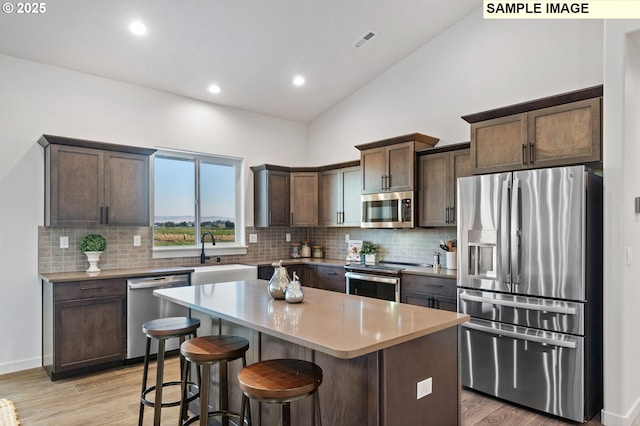 kitchen with a center island, sink, light wood-type flooring, dark brown cabinets, and stainless steel appliances