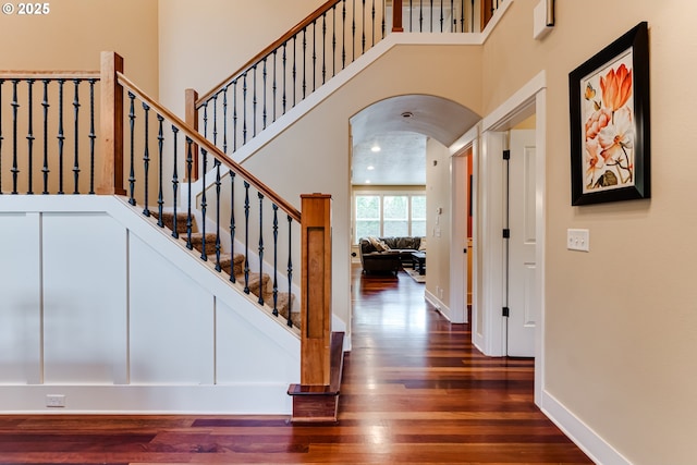stairs with arched walkways, baseboards, wood finished floors, and a towering ceiling