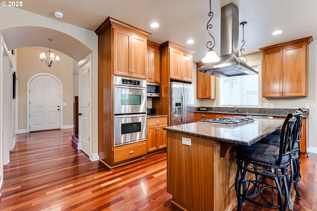 kitchen with arched walkways, a center island, stainless steel appliances, island range hood, and wood finished floors