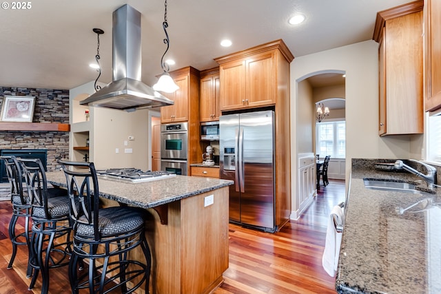 kitchen with a sink, light wood-style floors, arched walkways, stainless steel appliances, and island exhaust hood