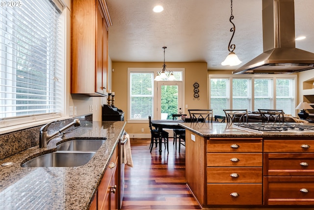 kitchen featuring brown cabinetry, dark wood-style flooring, island exhaust hood, a sink, and stainless steel gas stovetop