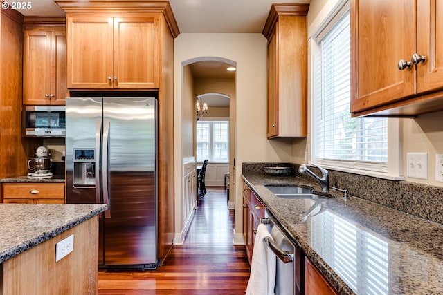 kitchen with a sink, appliances with stainless steel finishes, dark stone countertops, and dark wood finished floors