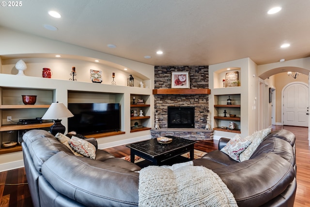 living area with built in shelves, arched walkways, and wood finished floors