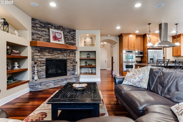 living area featuring baseboards, arched walkways, dark wood finished floors, and built in features
