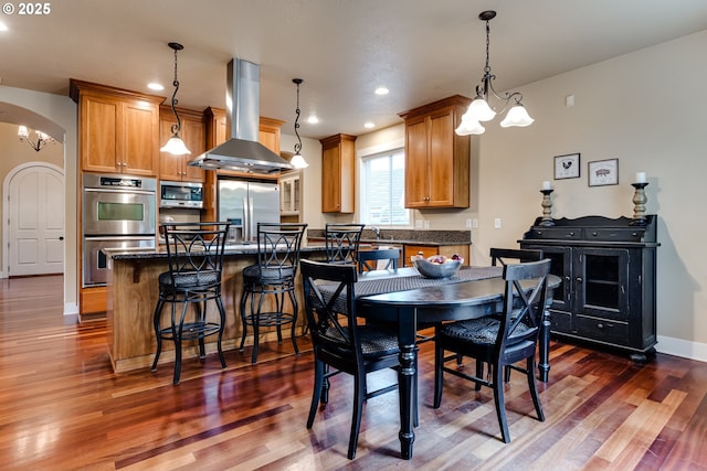 dining room featuring arched walkways, dark wood finished floors, baseboards, a notable chandelier, and recessed lighting