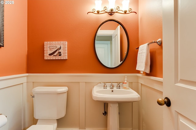 bathroom with a sink, a decorative wall, toilet, and a wainscoted wall