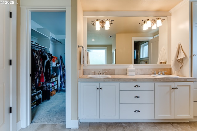 bathroom with double vanity, a walk in closet, an inviting chandelier, and a sink