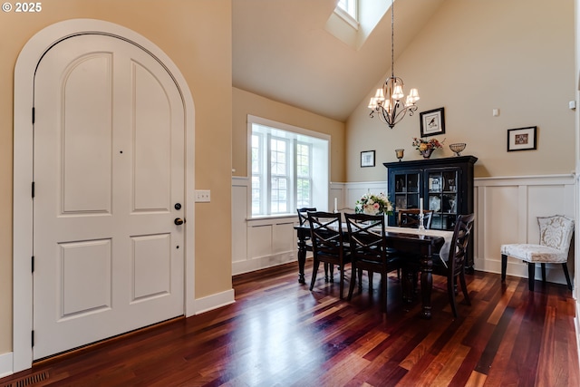 dining space with an inviting chandelier, a decorative wall, high vaulted ceiling, dark wood-type flooring, and a wainscoted wall